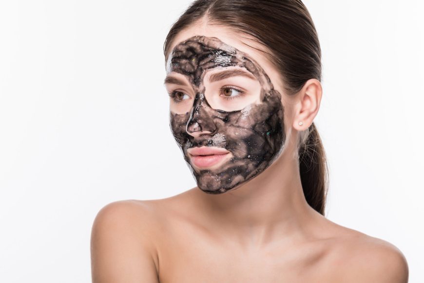 Beautiful woman with a clay or a mud mask on her face over white background